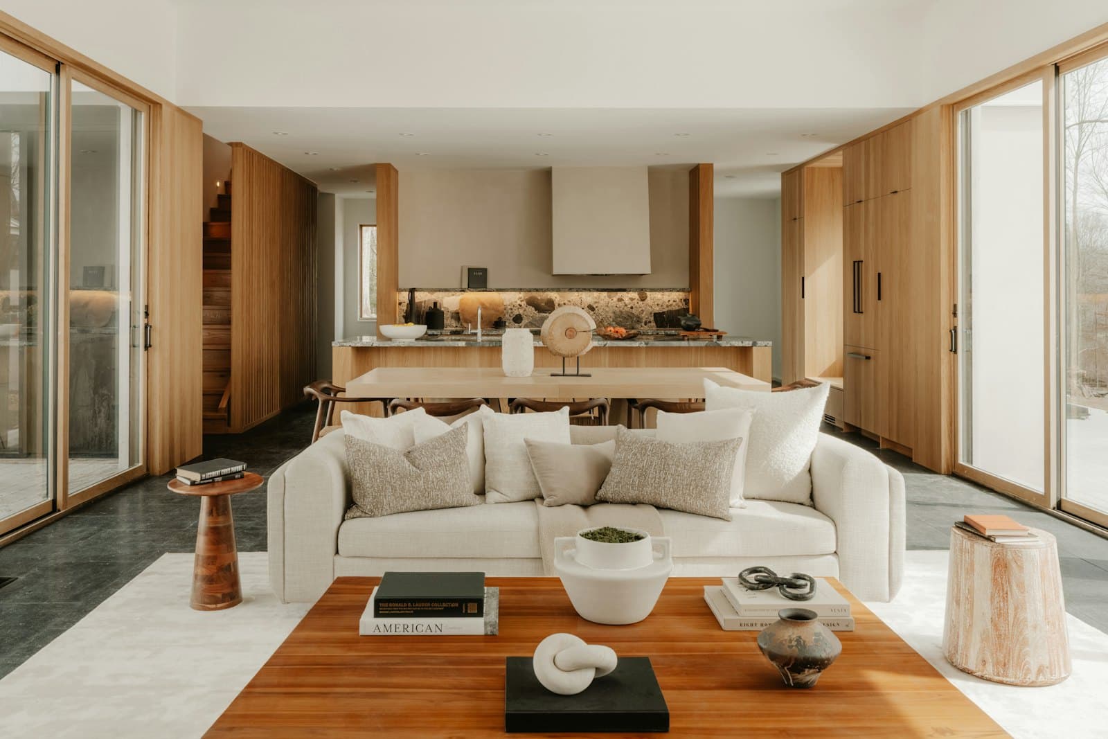 Bright open-plan living room with a cream sofa, natural wood cabinetry, and large windows. Illustrative stock photograph.