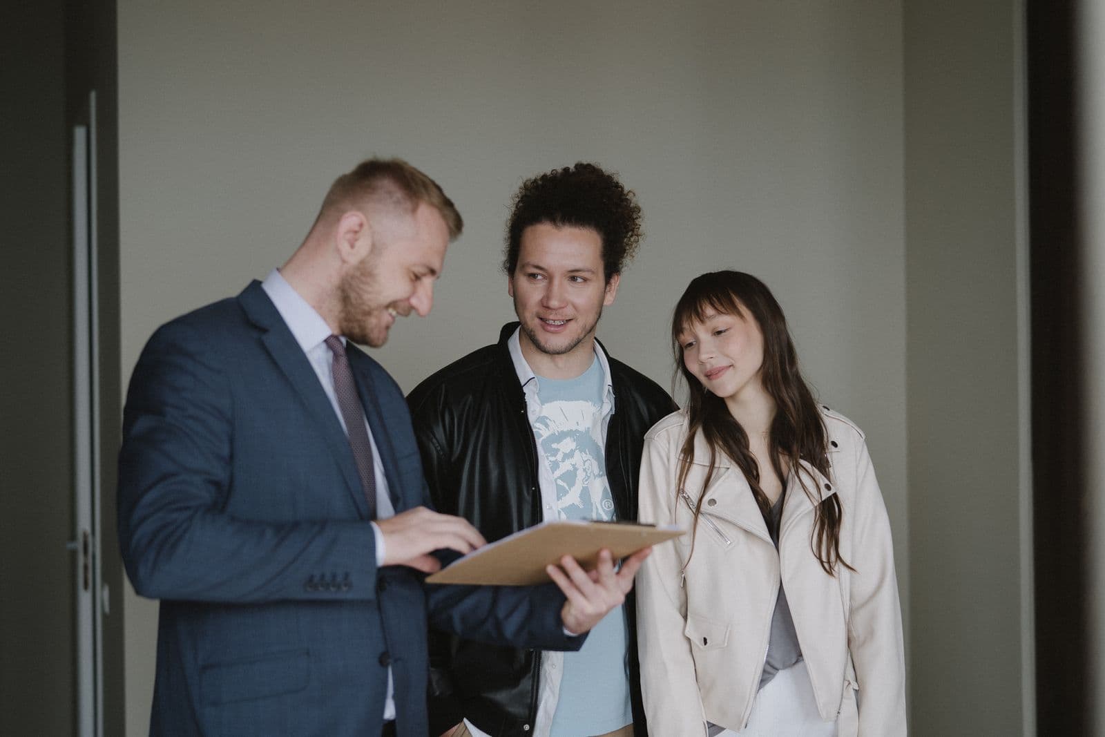 A couple reviewing a clipboard with a property professional during an indoor consultation. Illustrative stock photograph.
