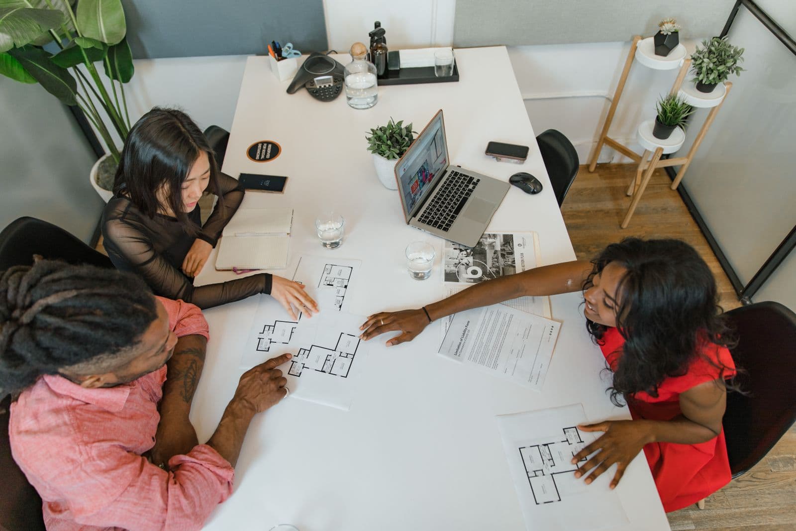 Three people reviewing floor plans together at a bright office desk. Illustrative stock photograph.