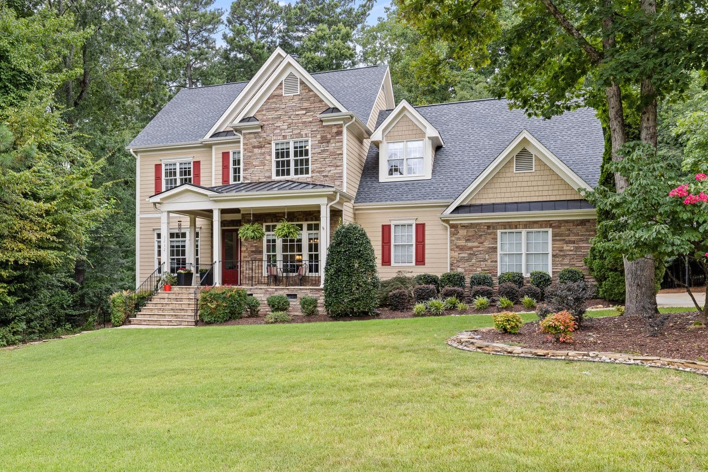 Two-story detached home with stone details, red shutters, and a landscaped lawn. Illustrative stock photograph.