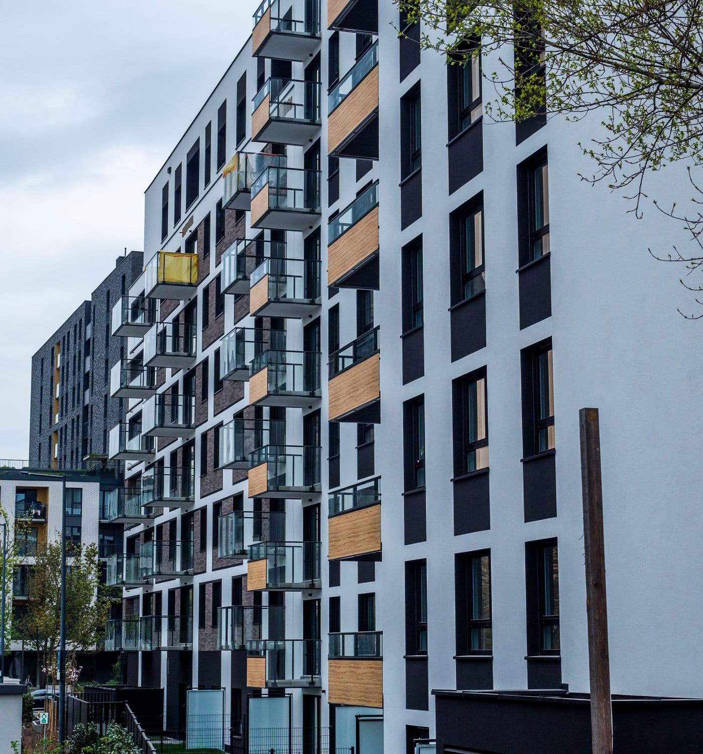 Modern apartment building with glass balconies, wood accents, and garden planting. Illustrative stock photograph.